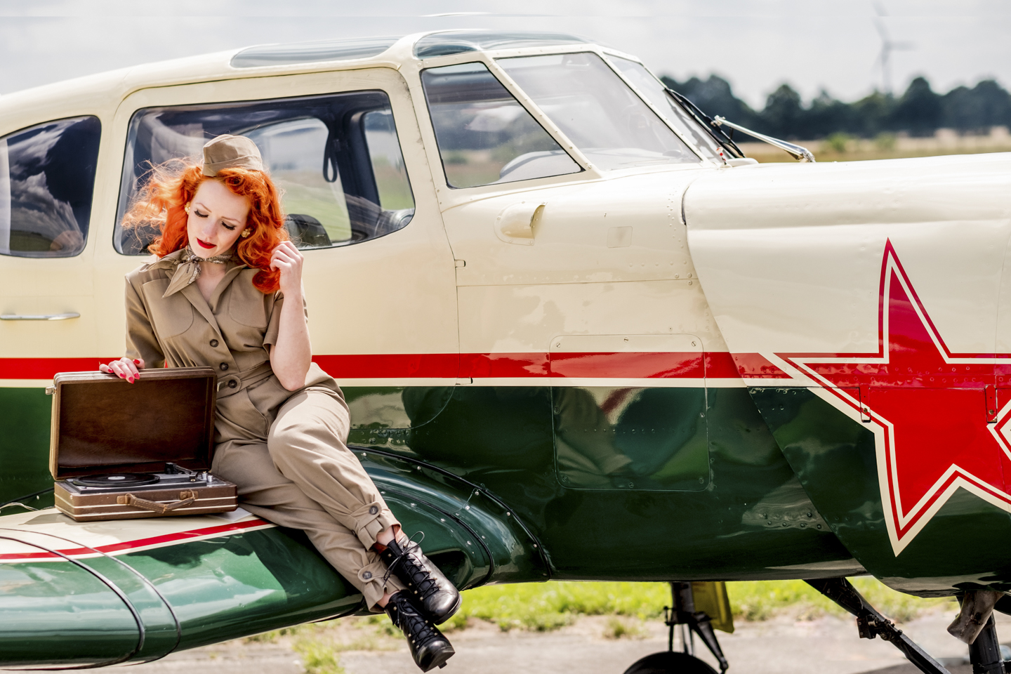 Rothaarige Frau mit beigefarbenen Pilotenanzug posiert auf dem Flügel eines kleinen Propeller Flugzeugs