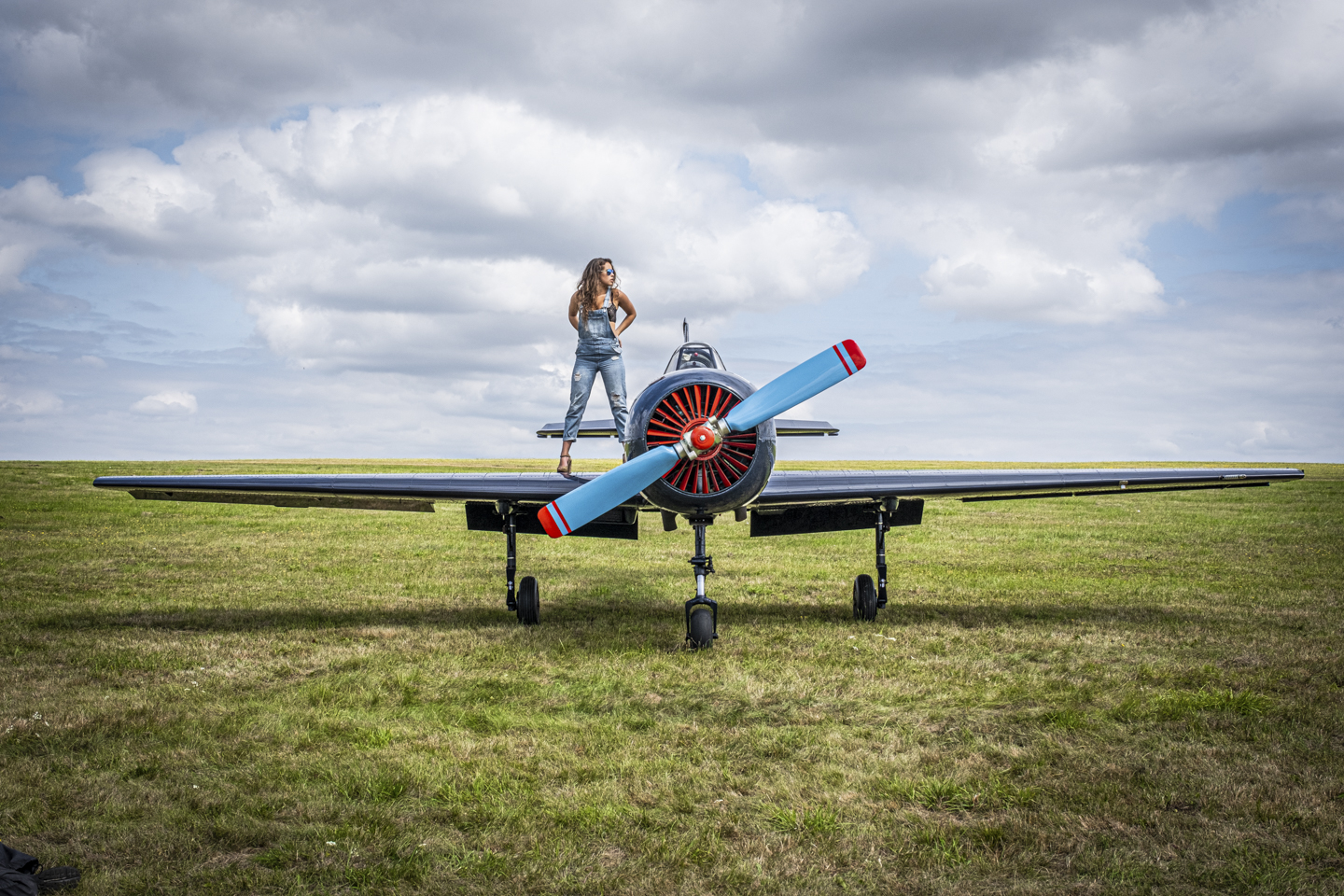 Frau mit Jeans Latzhose steht auf dem Flügel eines kleinen Propeller Flugzeugs