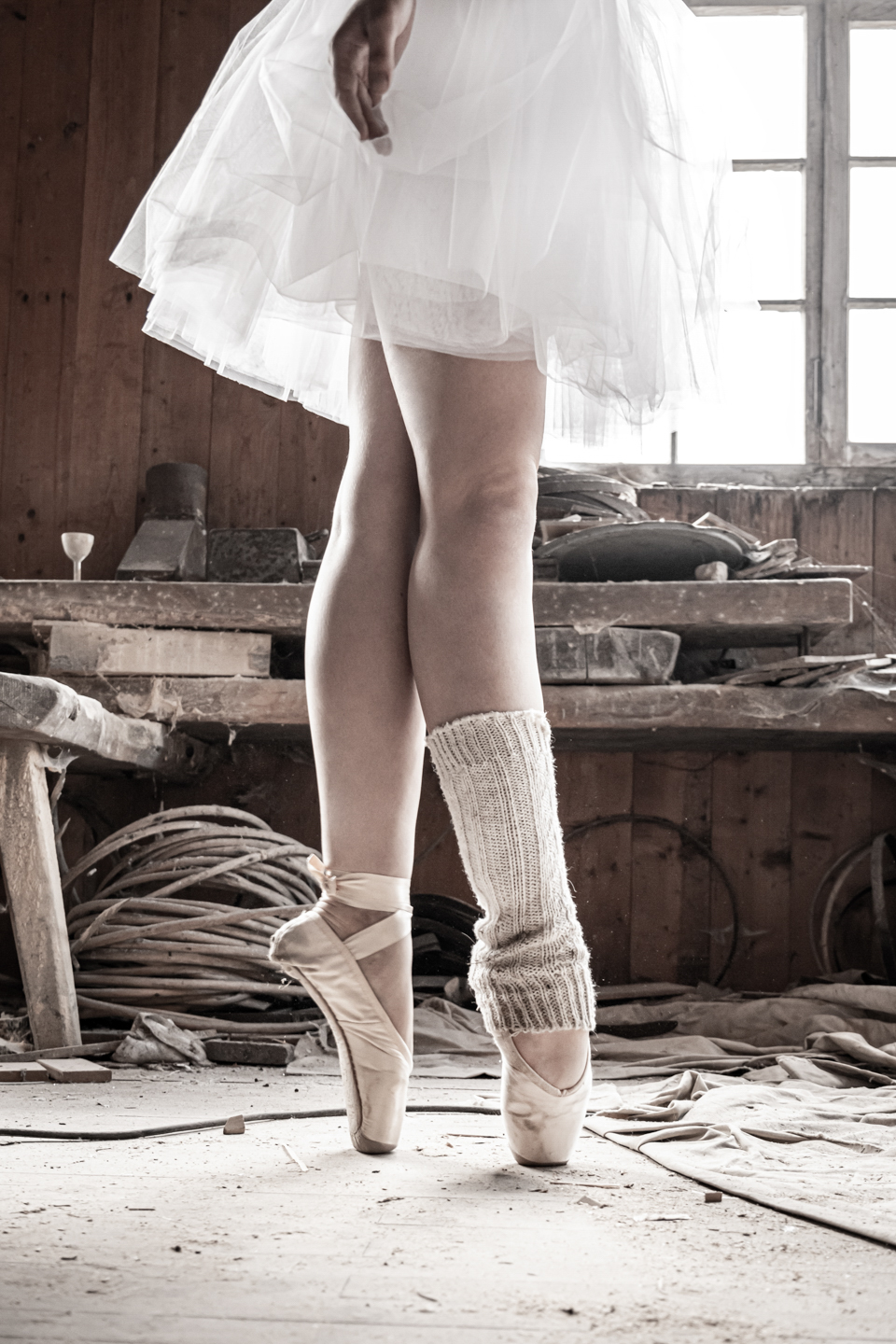 Beine einer Frau mit Ballettschuhen und Tüllrock in Ballettposition an einem verlassenen Gebäude