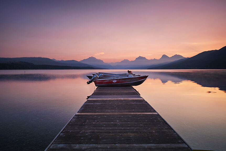 Small speedboats at the end of a jetty, with scenic lake and mountain background