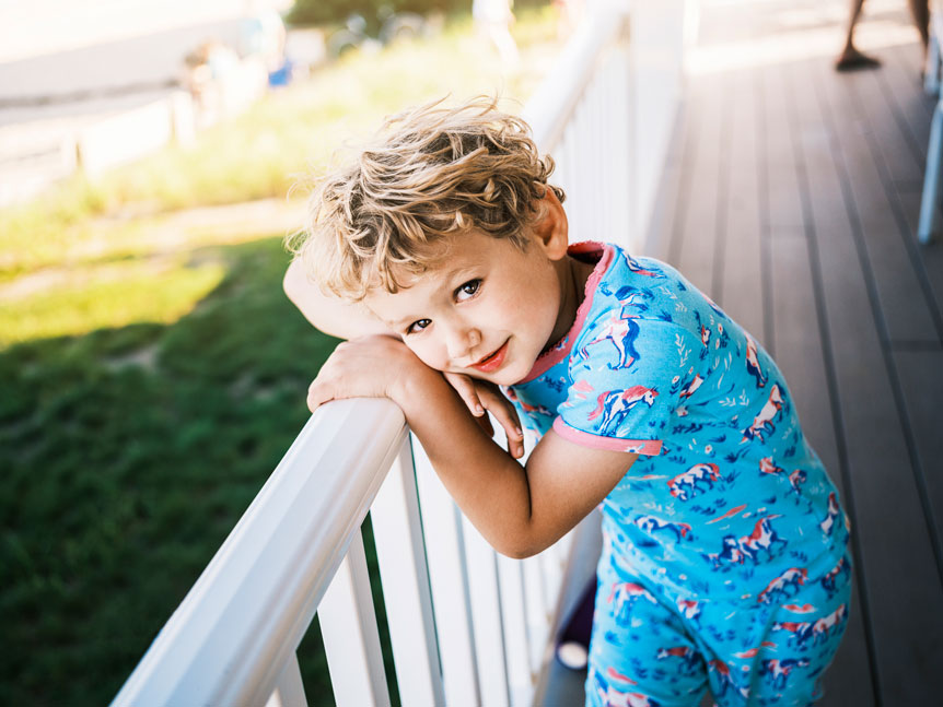Portrait of young boy leaning on the railing of a front porch on a sunny day