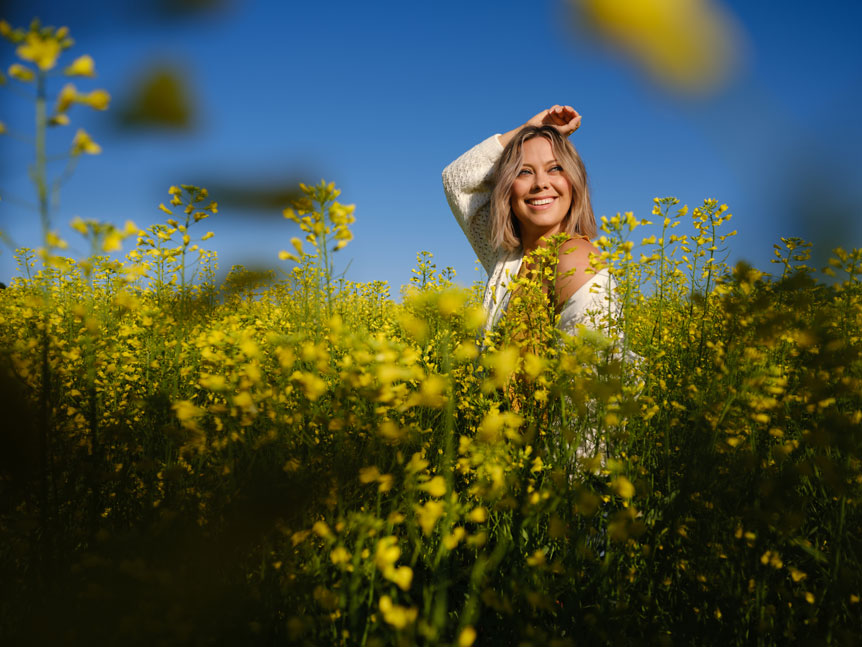 Woman posing among yellow flowers on sunny day against blue sky