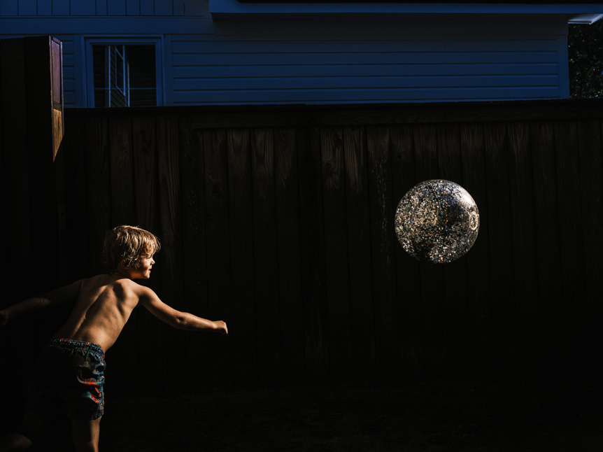 Boy playing with ball illuminated by golden sunlight against a background of dark shadow