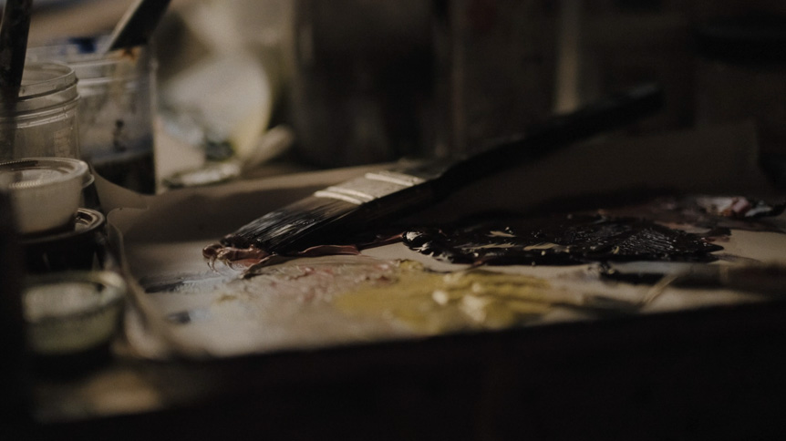 Videographer, Giulio Meliani uses FUJINON XF50mmF1.0 R WR to profile legally-blind artist, Therese Verner and show the importance of art. Image shows a video still of a paintbriush on a pallet alongside mixed yellow oil paint.