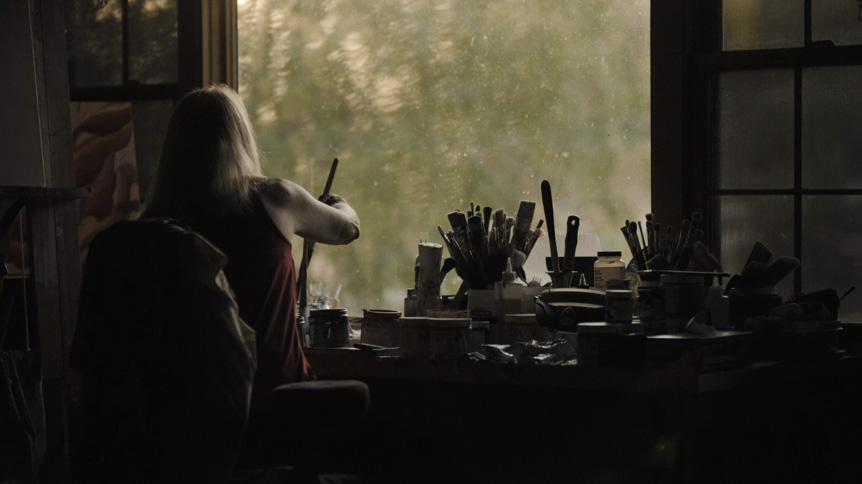 Videographer, Giulio Meliani uses FUJINON XF50mmF1.0 R WR to profile legally-blind artist, Therese Verner and show the importance of art. Image show a video still of Therese Verner working in front of a window in her studio