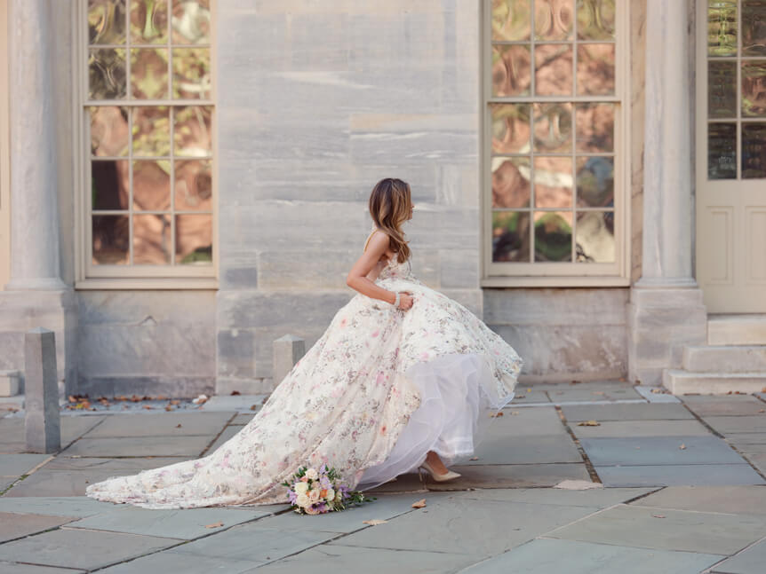 Professional photographer, Alison Conklin, on why the FUJIFILM GFX system is so good for location portrait photography. Image shows bride in her wedding dress walking past windows of a grand building with colourful reflections.