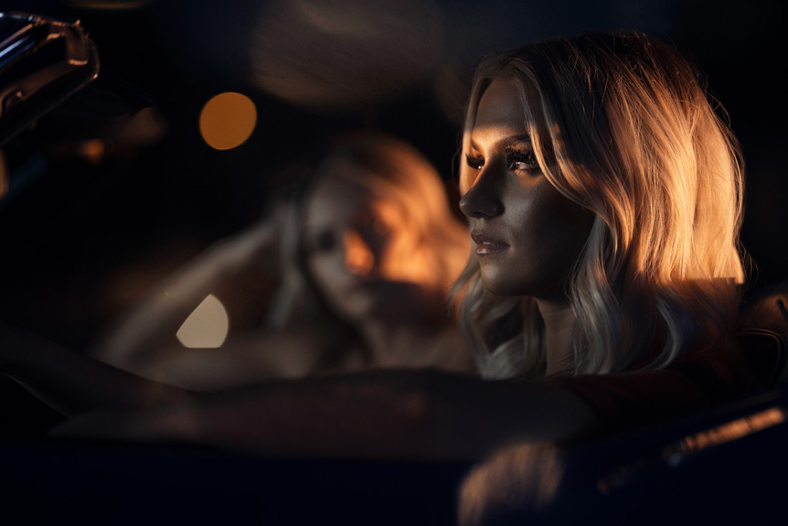 GFX System: The Power is in your Hands. Low light portrait of two women in a car, orange light from streetlight shines in to illuminate the subject's eyes.