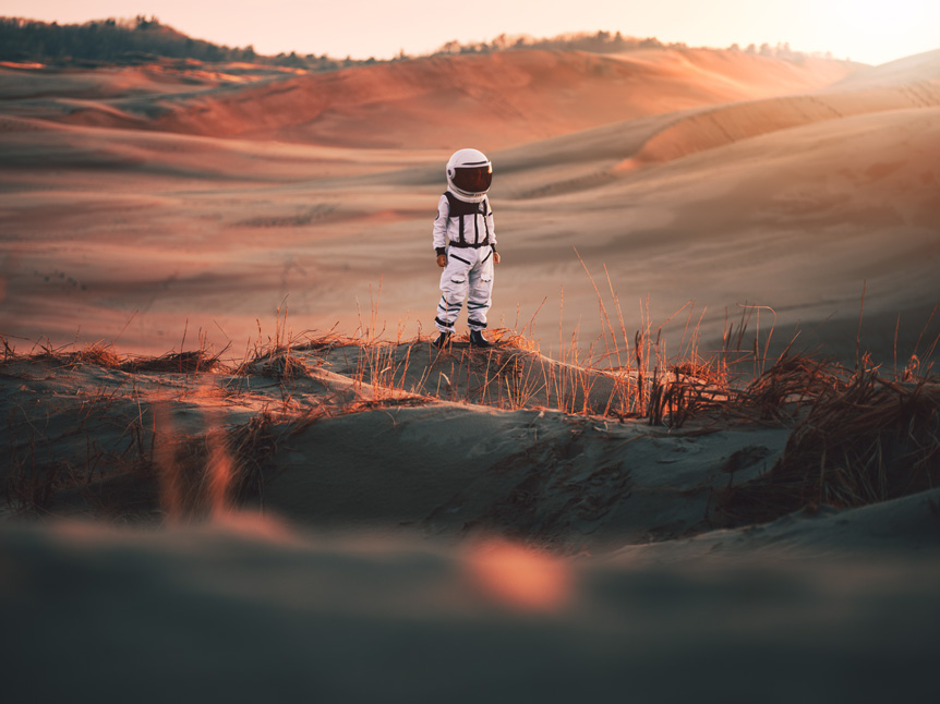 Boy dressed in astronaut costume standing in desert environment at sunset