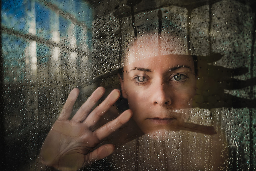 A young woman looks through a clear gap in a steamy window