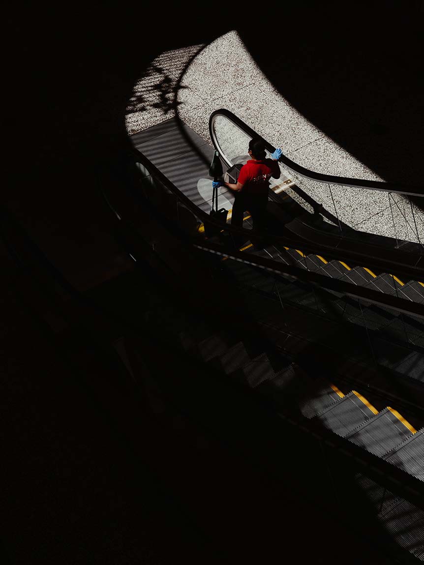 Person riding down escalator in ray of sunlight