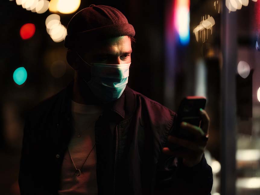 Young man in mask looking at his phone on dark street