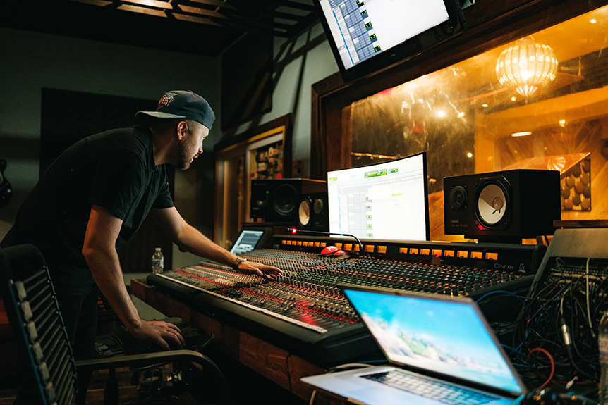 Music producer in front of control panel and colorful booth