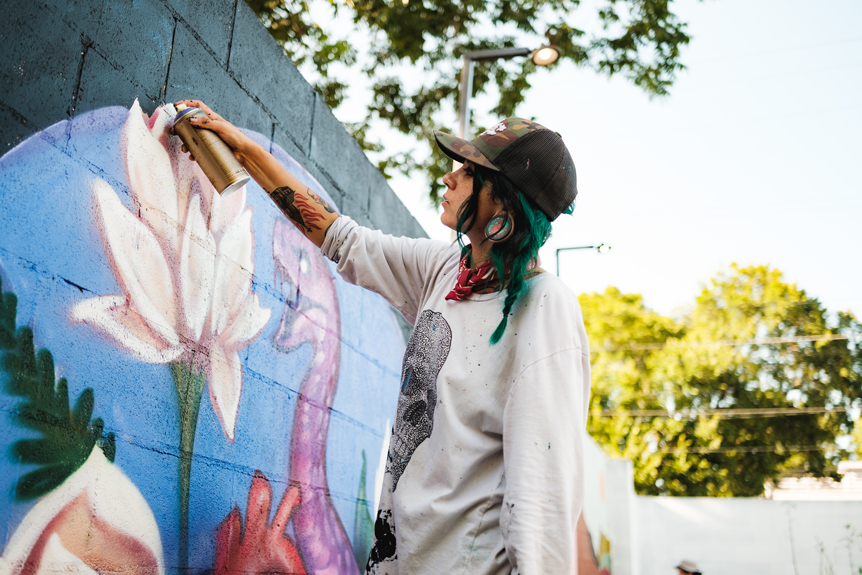 Woman with blue hair spray painting a wall