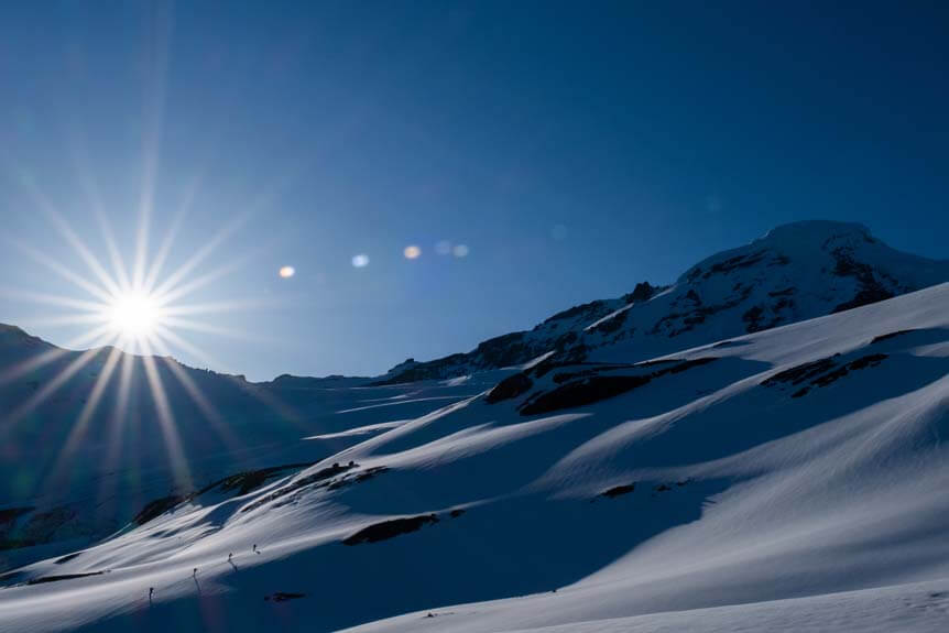 A luminous sun cuts through an icy landscape of snow dunes