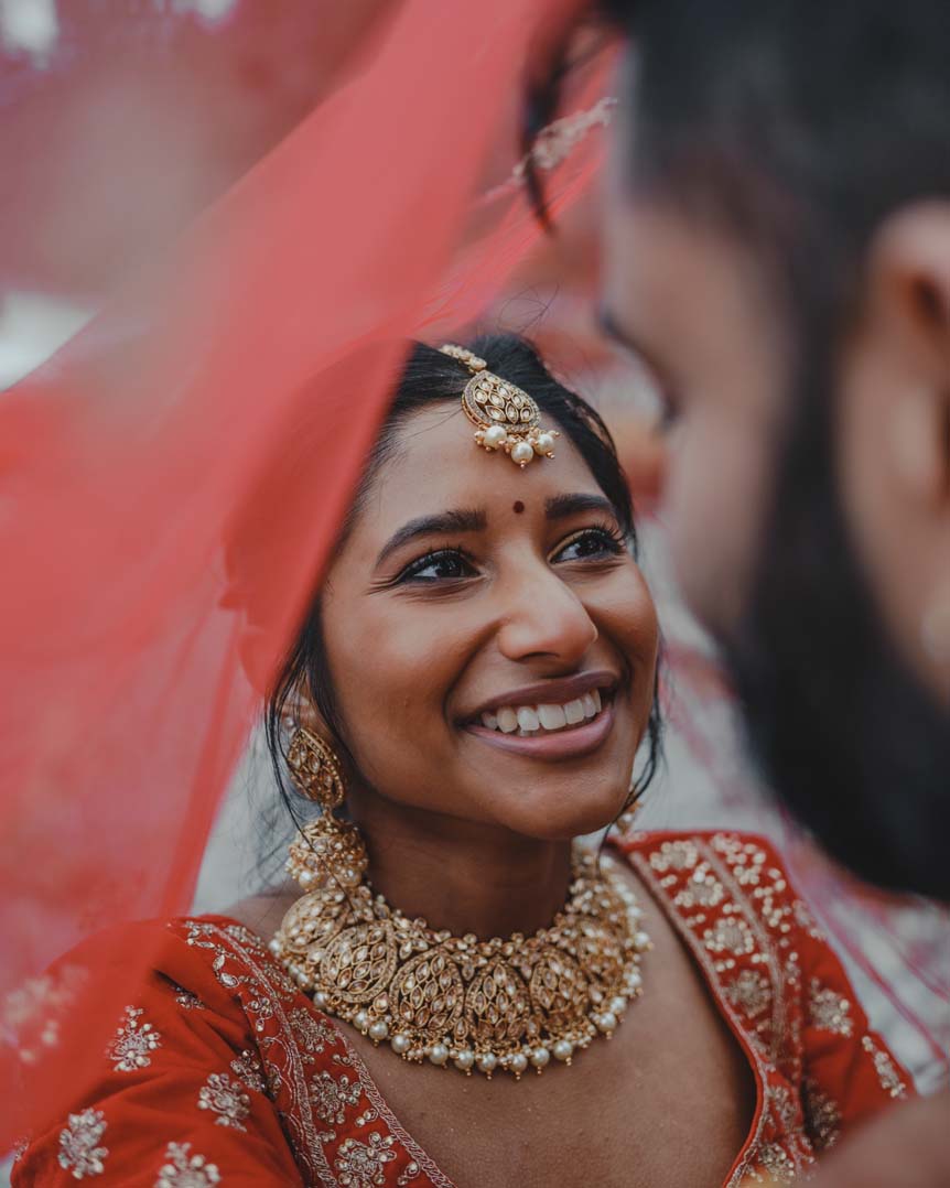 An Indian couple share a happy moment together beneath the bride's wedding veil
