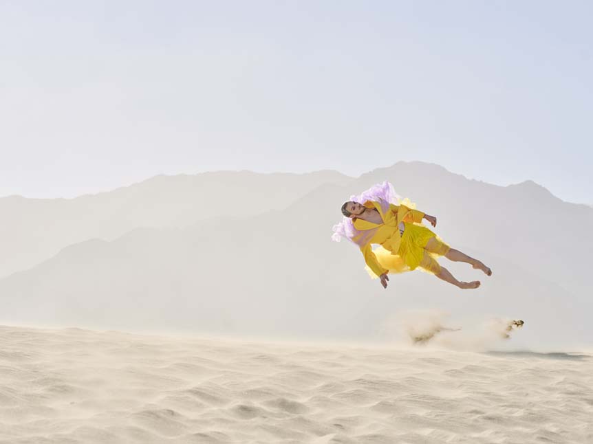 A man in a banana chiffron suit-dress comically flies through the air