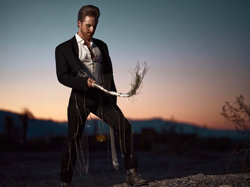 A man with a slick pompadour hairstyle poses against dusk in Death Valley