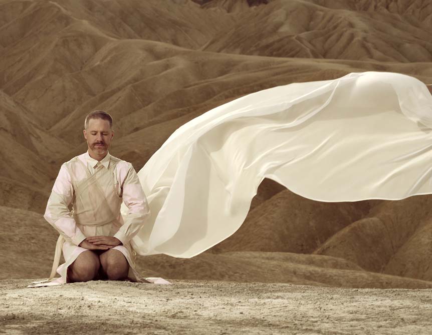 A man meditates upon the hot sands of Death Valley, draped in a white flowing gown