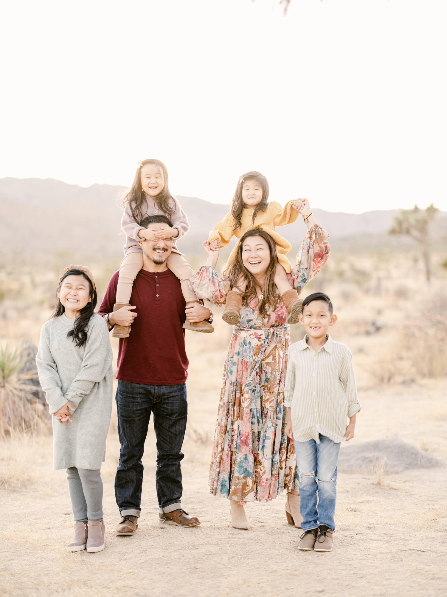 An Asian family of six playfully pose for a portrait, framed amongst sprawling desert surroundings