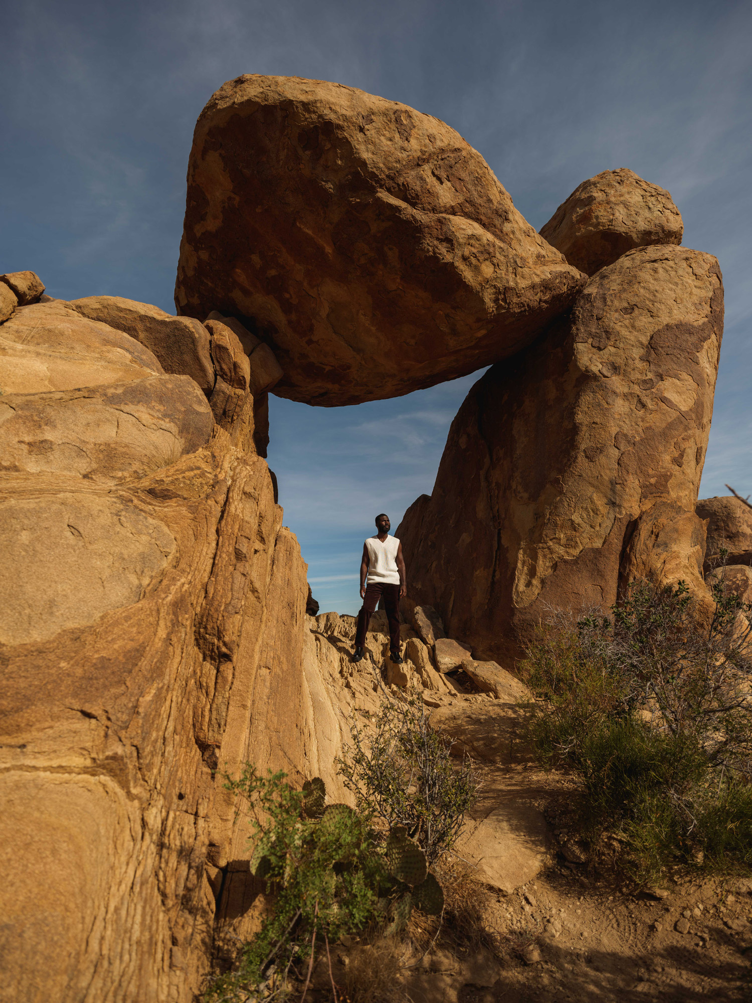 An African American man stands beneath a large rock, perfectly balanced between two parallel pillars of stone