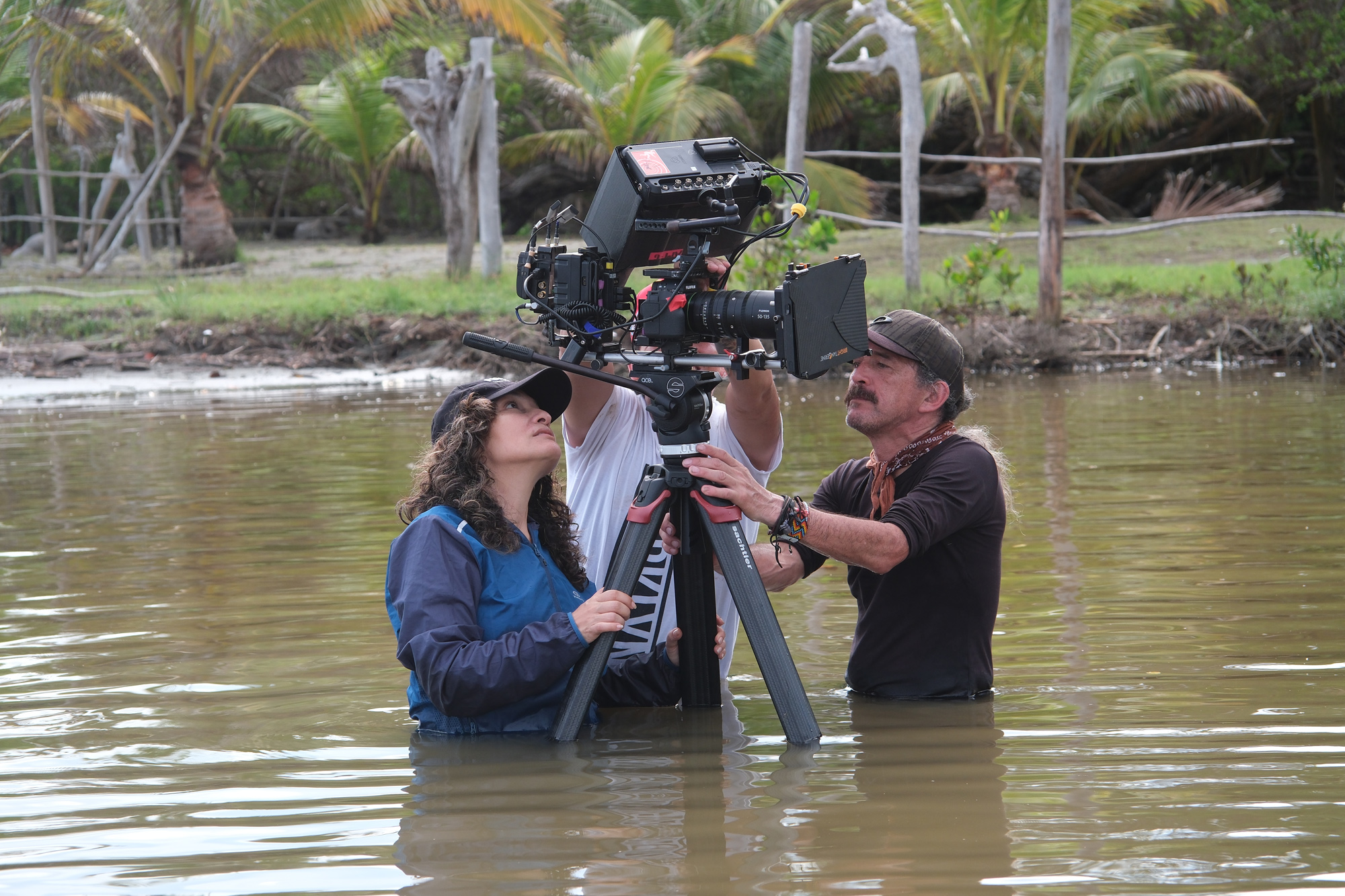 Two people stand submerged in lake water from the waist down, tampering with the controls of an X-H2 camera