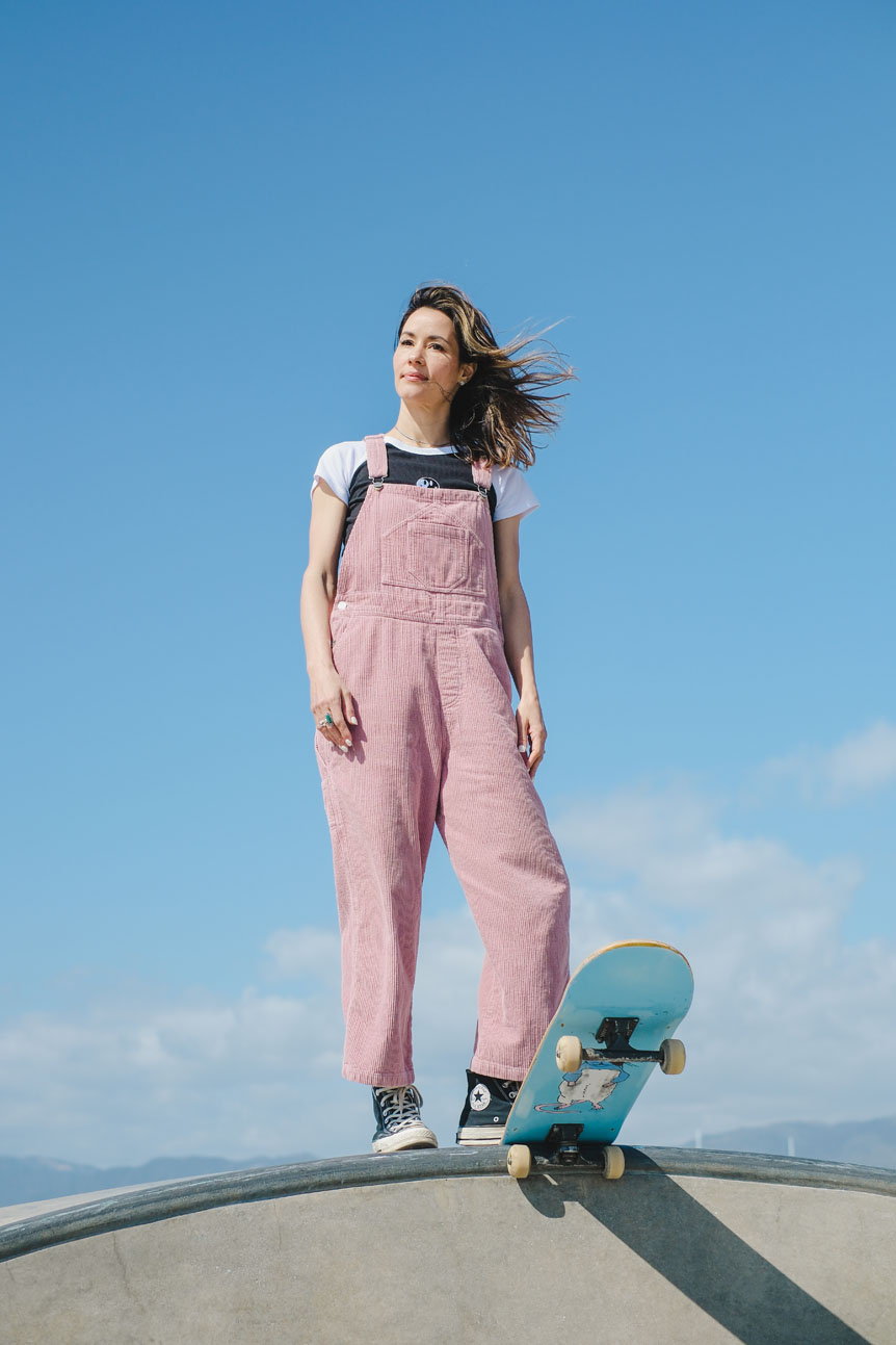 Young woman in pink jumpsuit standing at the top of ramp with skateboard