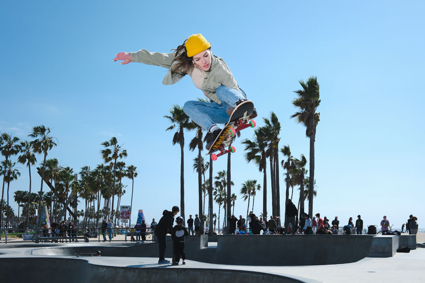 Young woman skateboarder performing board grab in mid air on California skatepark ramp