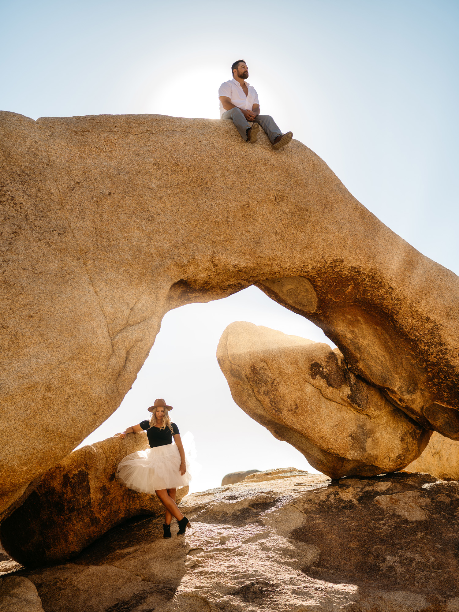 Man sitting atop huge natural stone arch with woman beneath