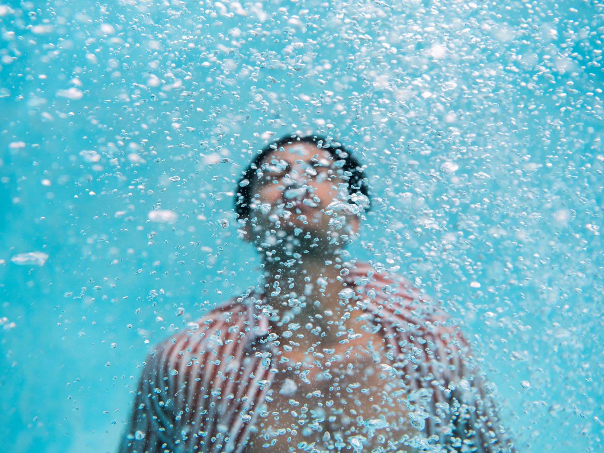 Submerged underwater, a man is surrounded by a peppering of bubbles