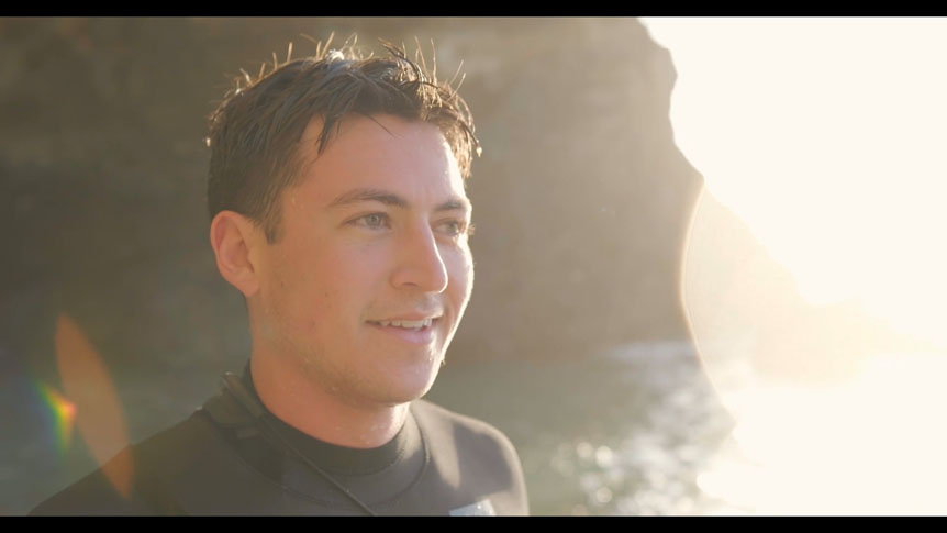 Young man on rocky shore in golden sunlight