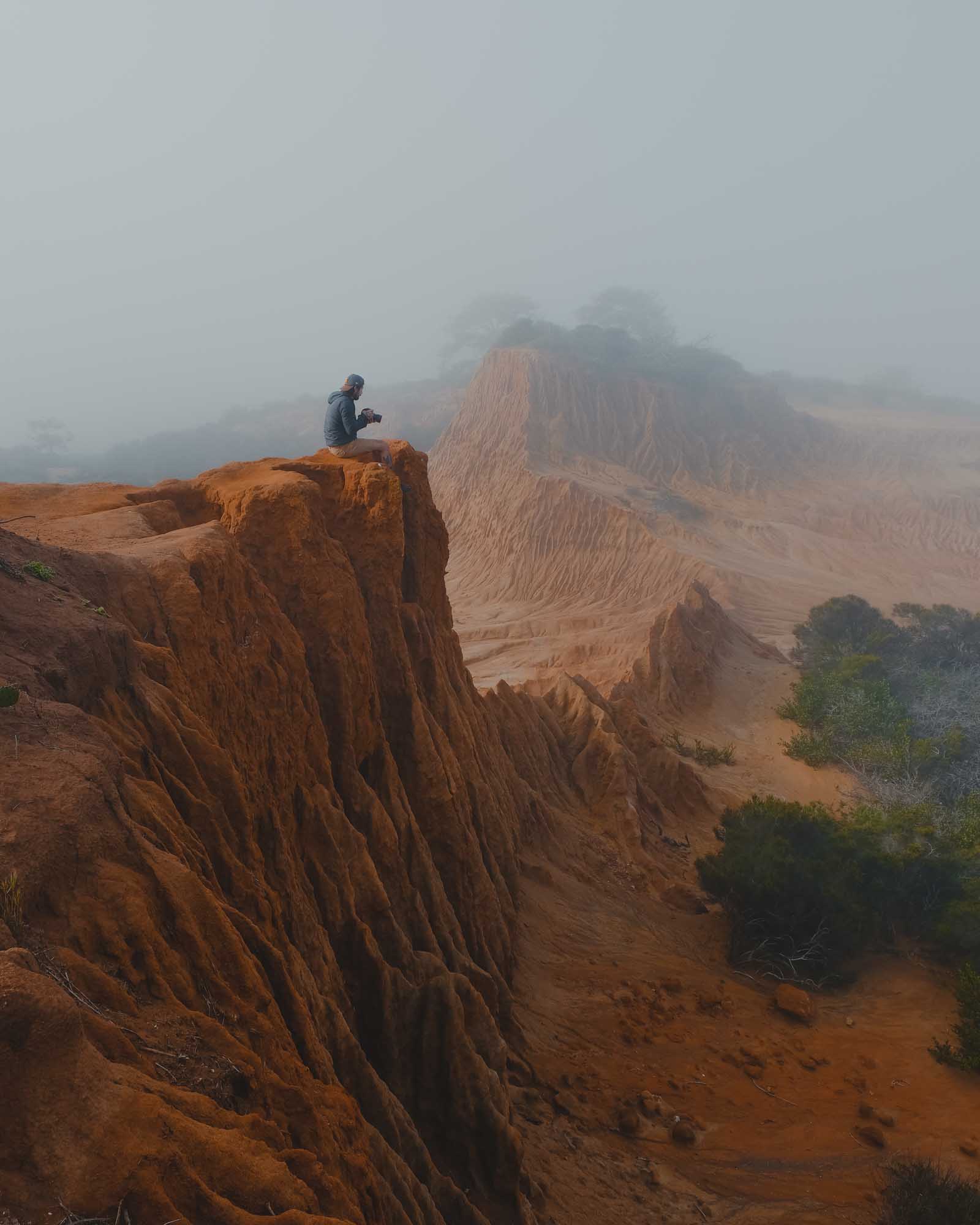 A man sits on the edge of a sandy cliffside