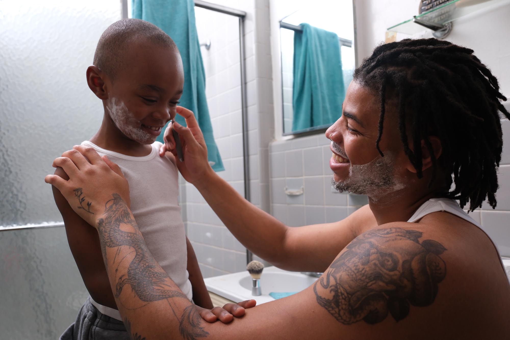 An African American father playfully shaves his son