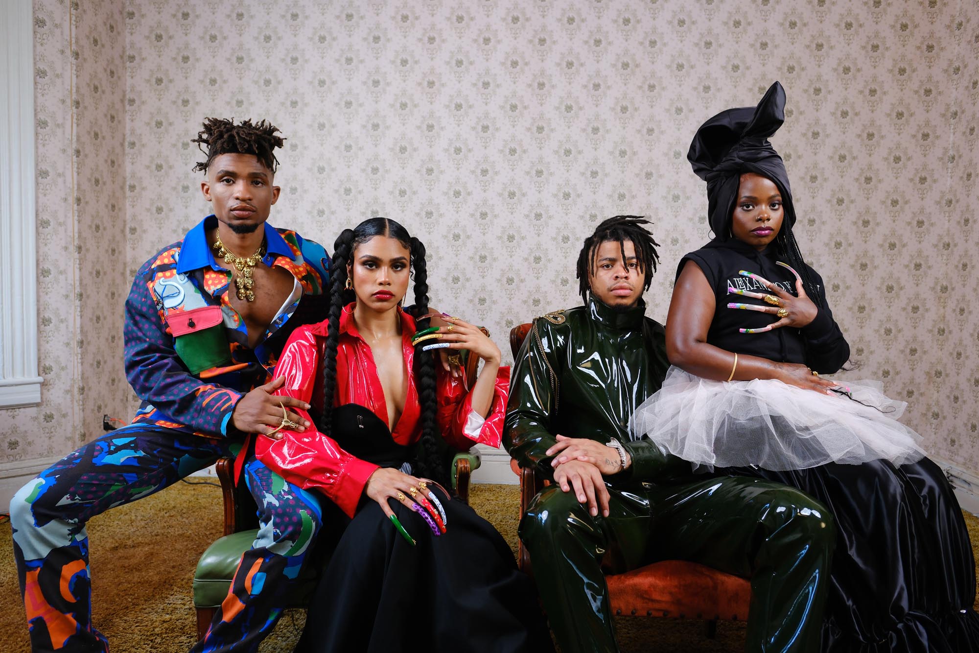 Four young African Americans pose in extravagant garments, framed against a drab wallpaper