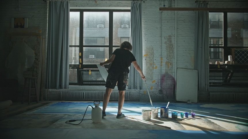Older woman artist painting huge canvas on floor of studio