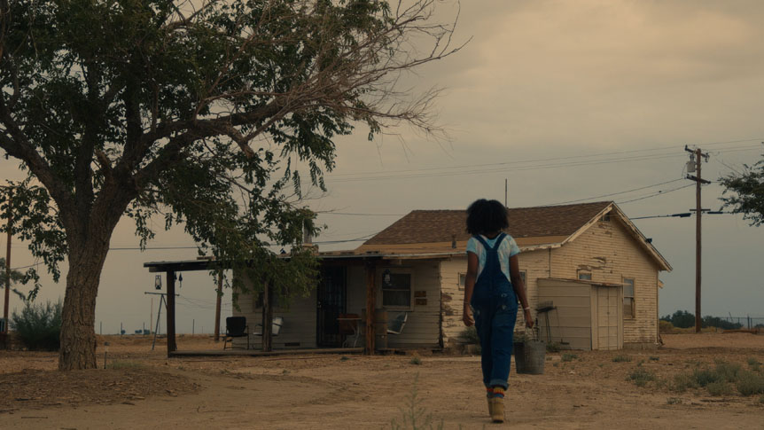 Young girl carrying water towards small desert house