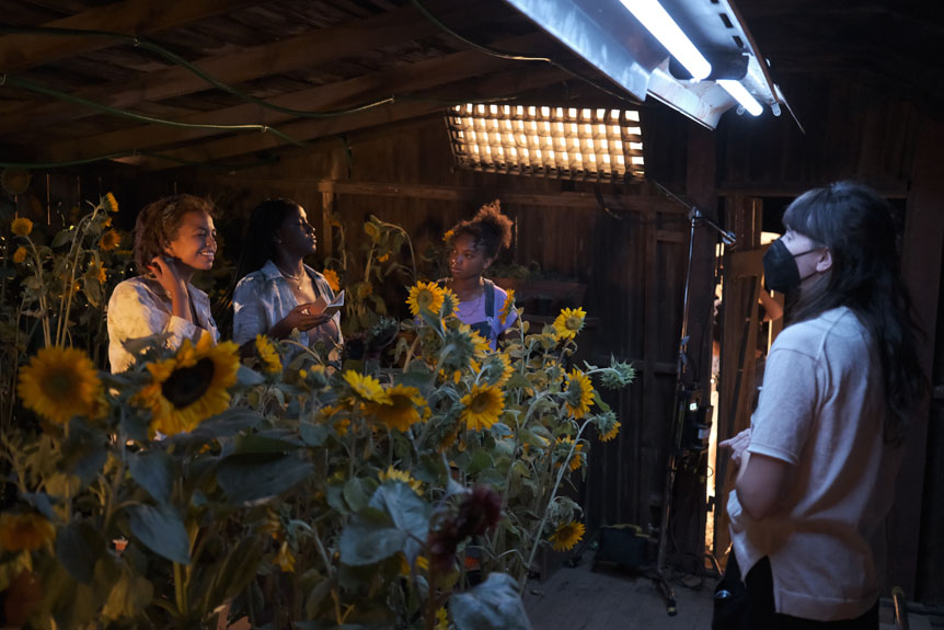 Director and young actress performing camera test inside barn full of sunflowers
