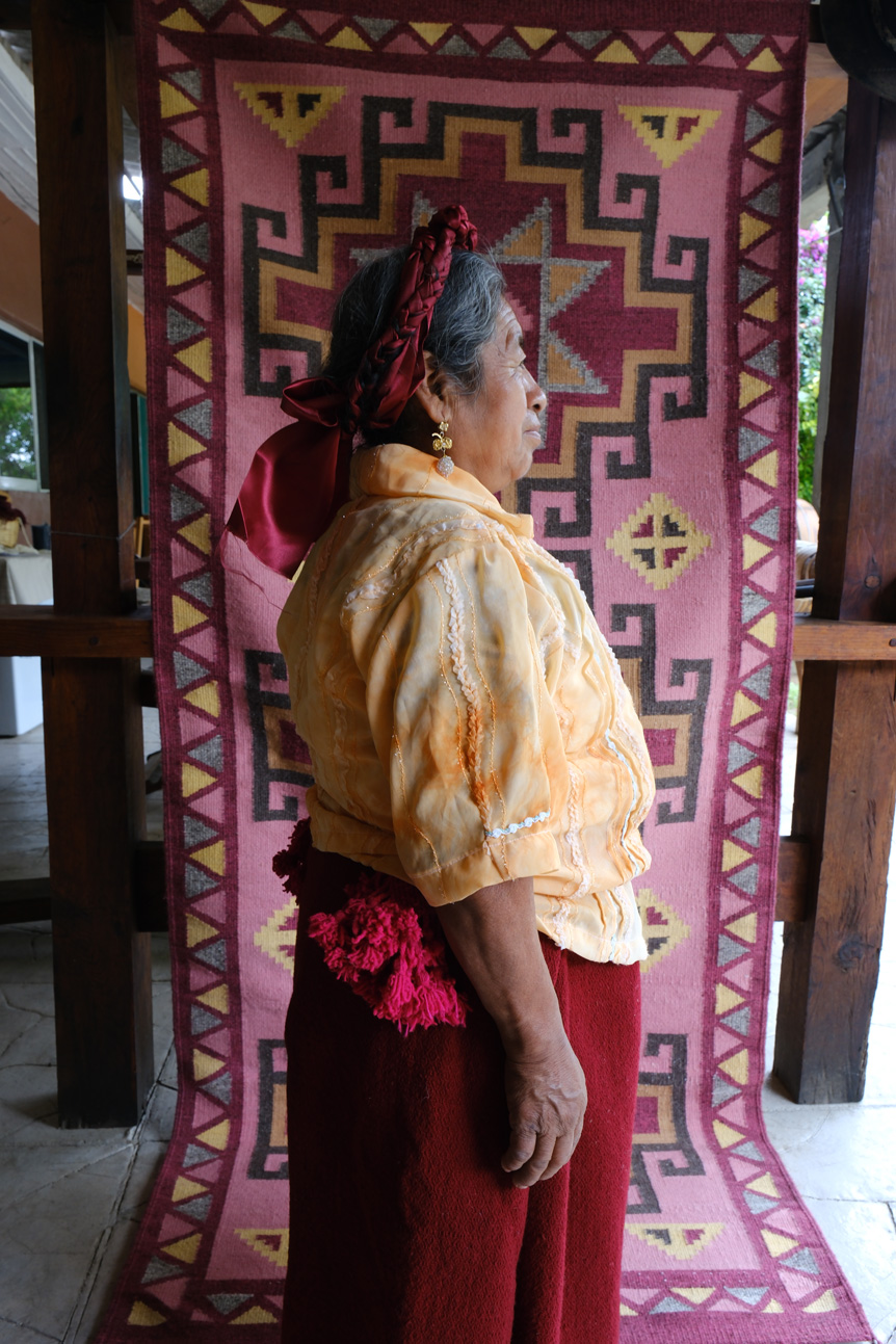 Elderly Oaxacan woman posing in front of traditional woven rug