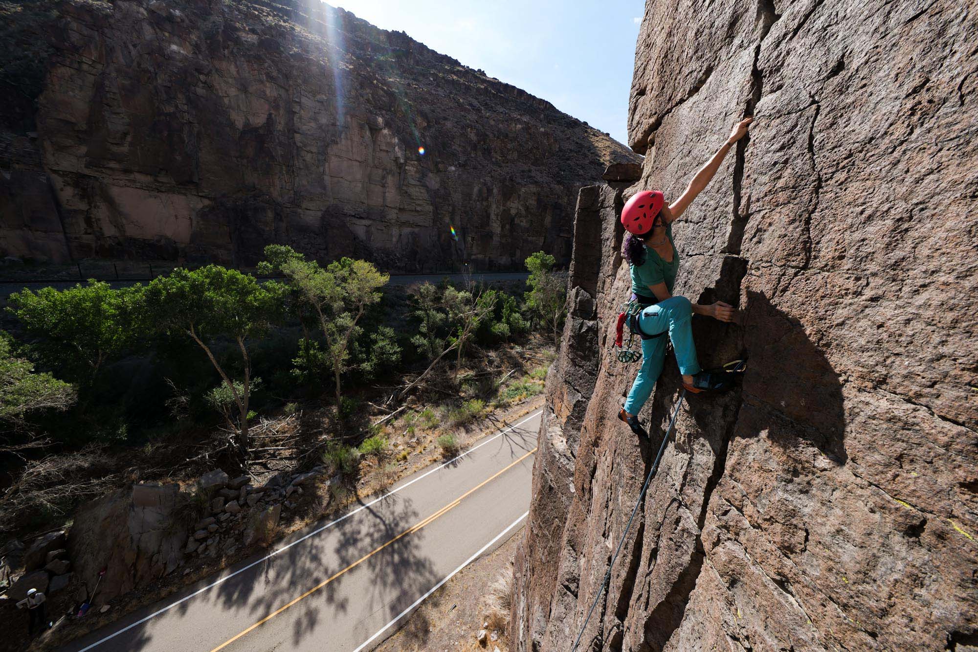 Framed against a winding highway, a woman scales a rocky cliff