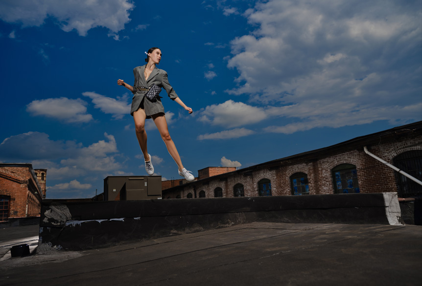 Young woman fashion model photographed mid jump on flat building rooftop