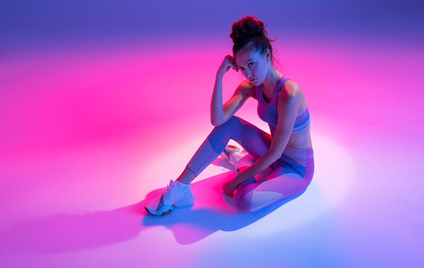 Young woman fitness model wearing sports clothing under purple studio lighting