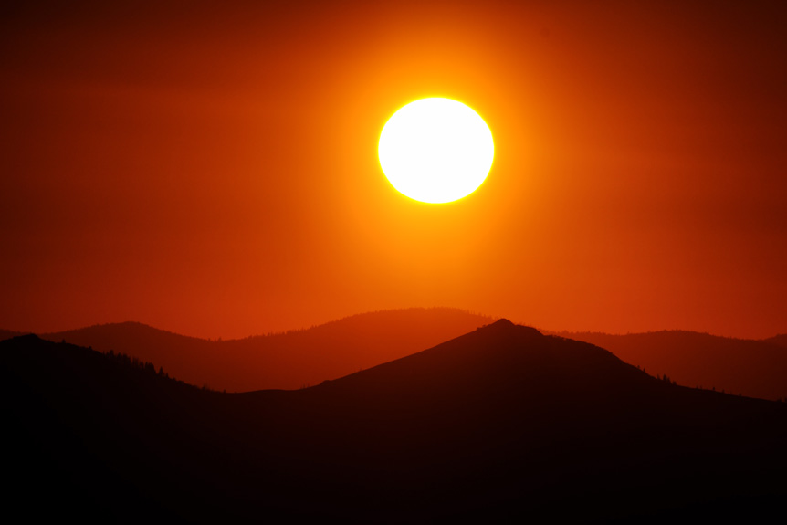Orange sun and red sky behind silhouette of mountains