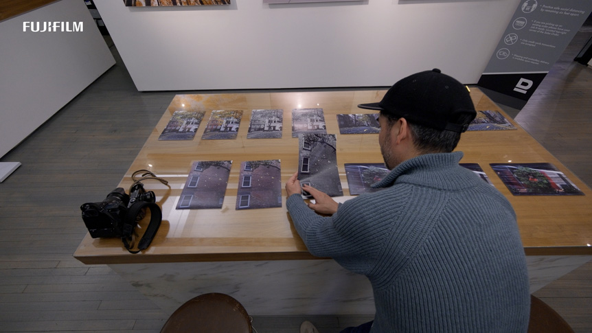 Male photographer sitting at table inspecting a number of printed photos that have been laid out on the table top