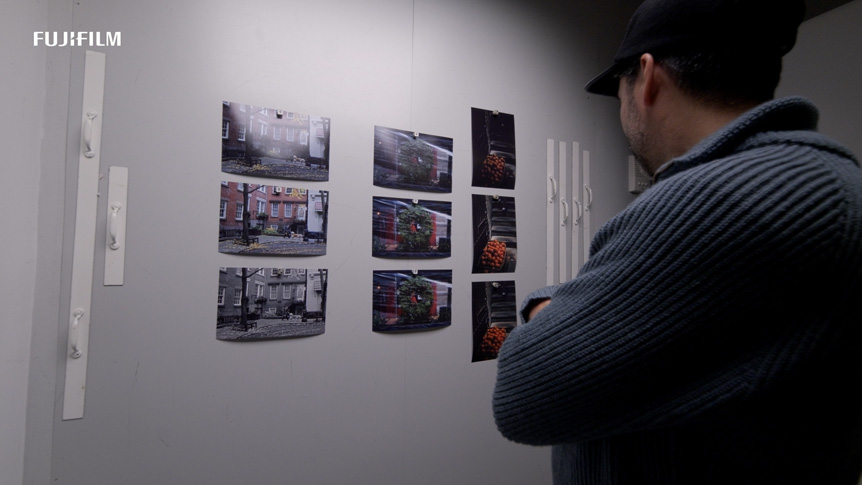 Over-the-shoulder shot of man inspecting printed photographs that have been attached to a white wall for viewing