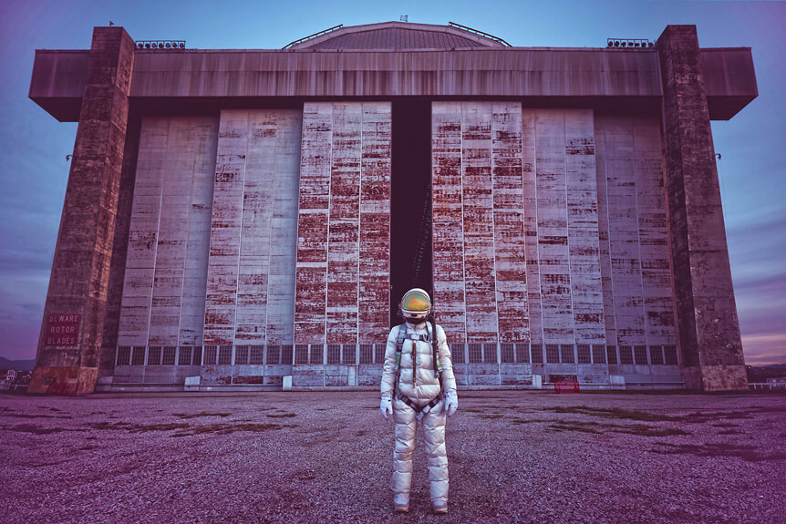 Astronaut standing in front of huge sliding doors of abandoned blimp hangar