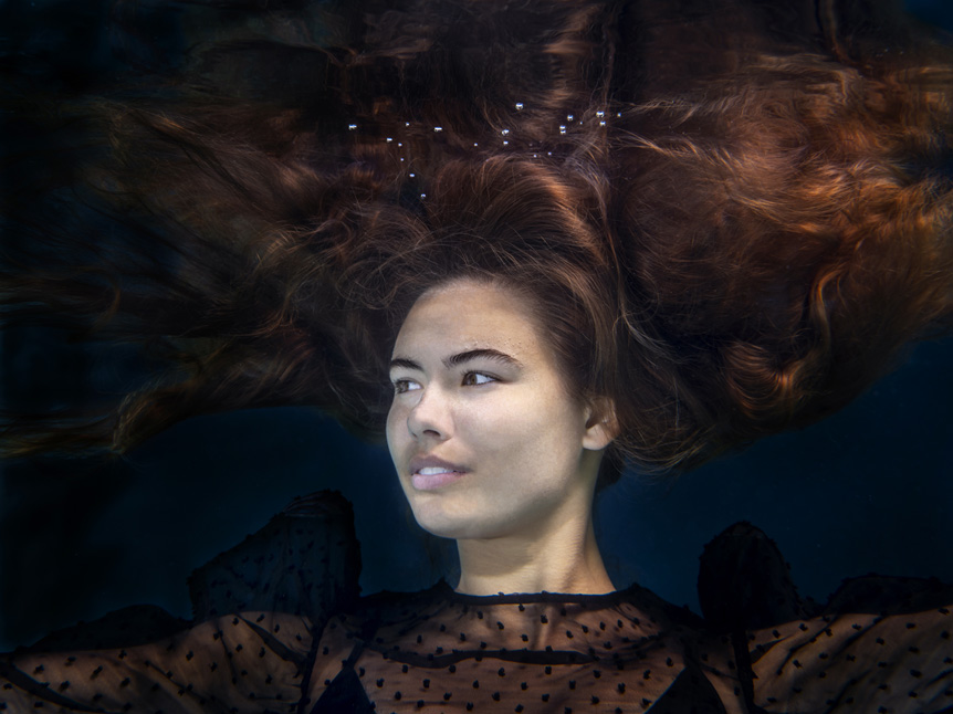 Young woman with long hair drifting under water