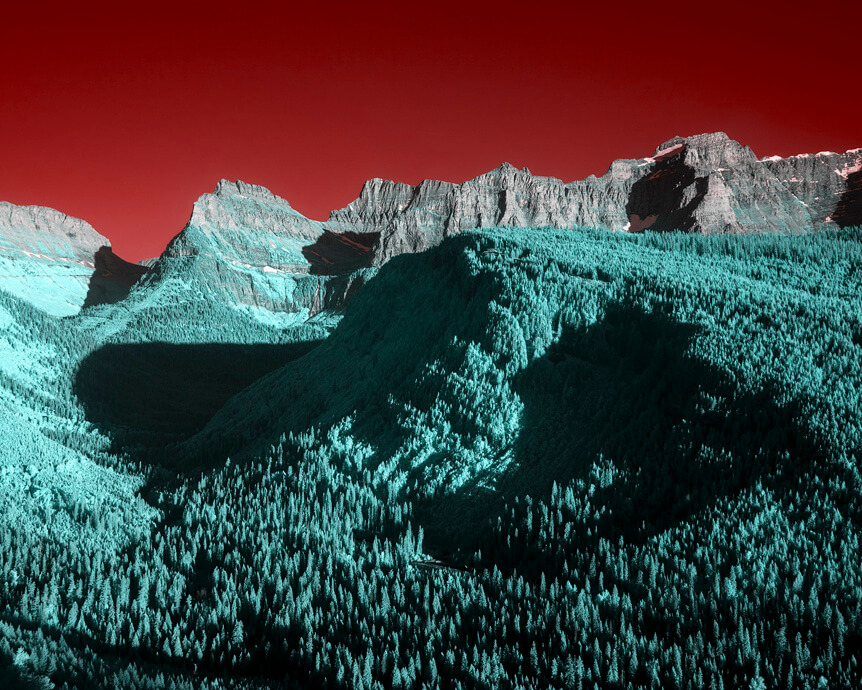 Dense teal forest leading to mountain, under red sky