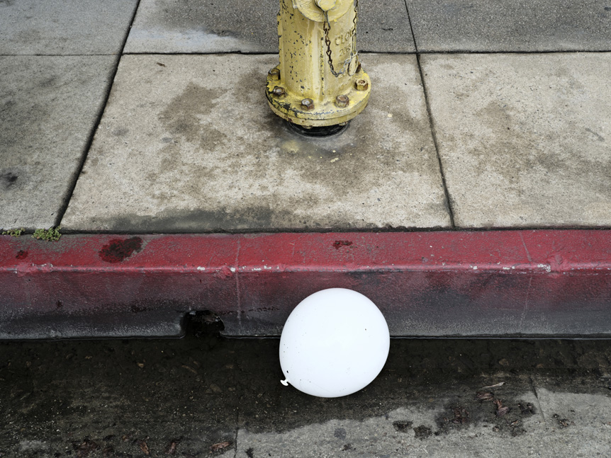 Image of white balloon discarded on a street in the gutter near a fire hydrant