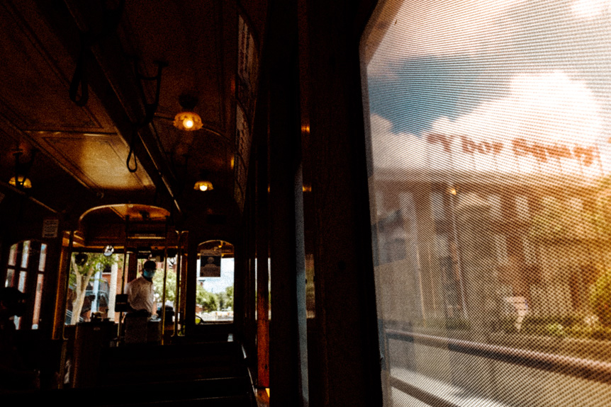 Image taken from inside a tram or train looking out of the window at a building with signage fixed to its roof.