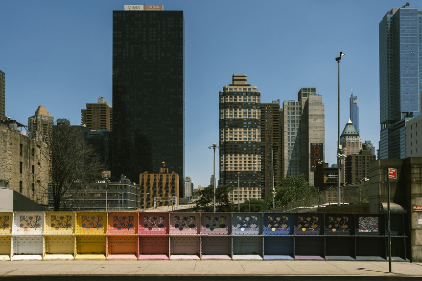 Rainbow-painted guard rail with New York City skyline beyond