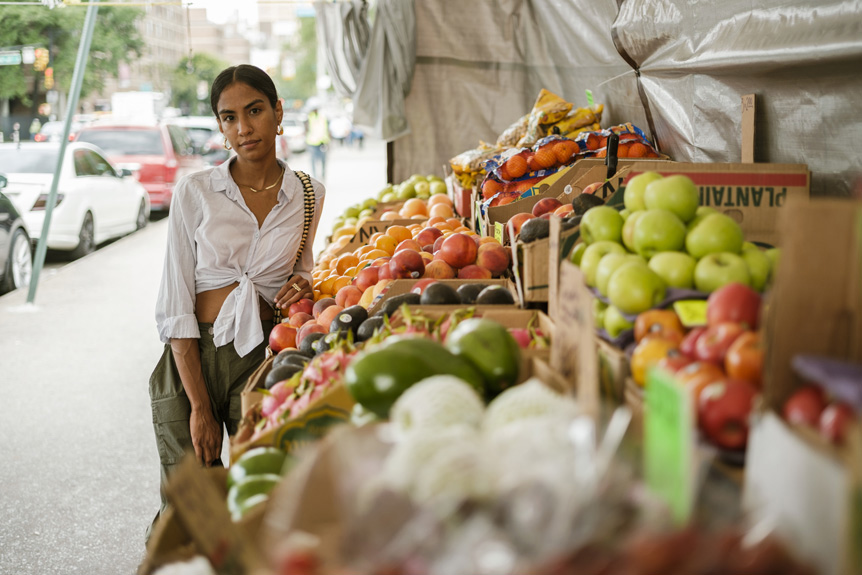 Young Latin woman posing against vibrant fruit and vegetable stand on New York City street